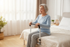 Elderly woman sitting on bed edge gripping handrail